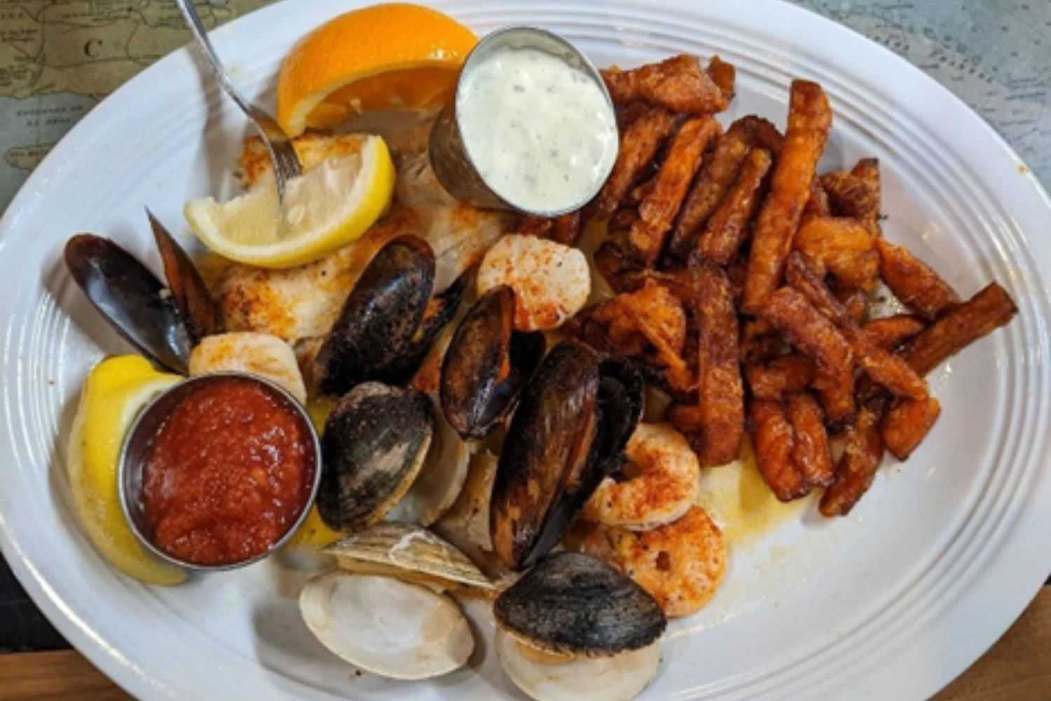Seafood platter with lemon wedges, dipping sauces, and sweet potato fries.