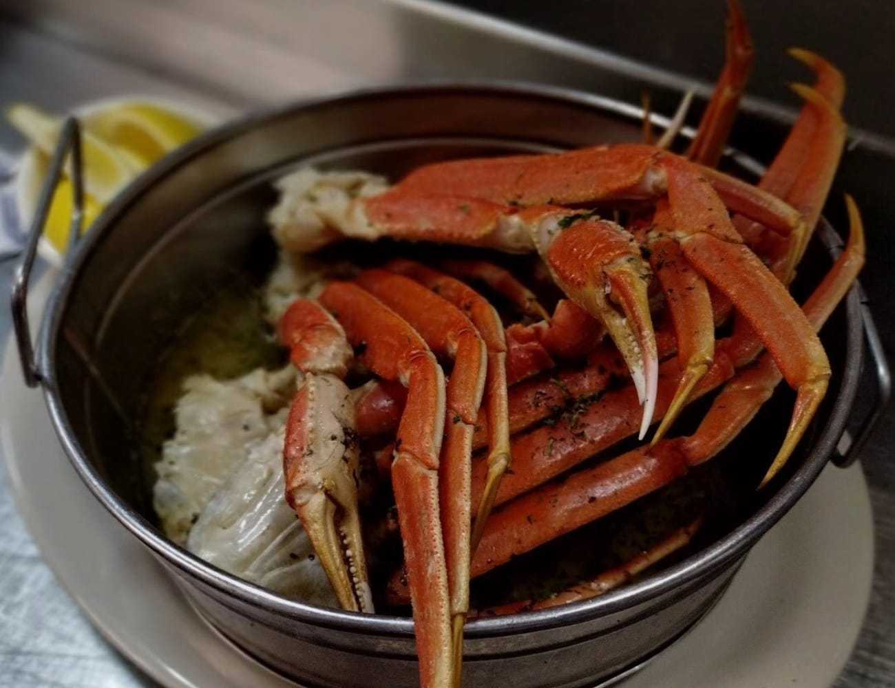 Steamed crab legs served in a pot with lemon wedges on the side.
